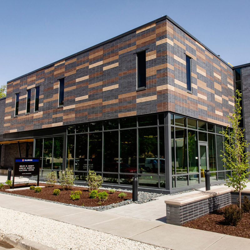 A rectangular black and brown brick building with large glass windows. 