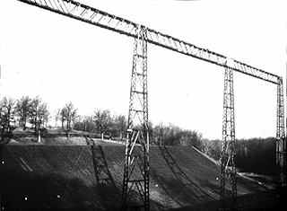 University of Illinois radio telescope used to map extra-galactic sources, a 400 x 600 foot cylindrical parabolic reflector made by covering a shaped-earth excavation with asphalt and wire screen. A catwalk at 155 feet above the ground supports about 400 conical log-spiral antennas along the focal line. Scanning in one plane was achieved by the earth's rotation; in the other plane by physically rotating the circularly polarized spirals. The log-spiral antennas were designed by Prof. J. D. Dyson, the feed system was designed by Prof. Y. T. Lo.