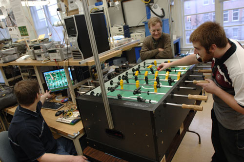 Steve Havlir (seated) and James Cavanaugh (right) demonstrate the &amp;ldquo;Automatic Foosball Table,&amp;rdquo; just one of the intriguing projects under construction this semester in the Advanced Digital Systems Lab. Course instructor Lippold Haken looks on.