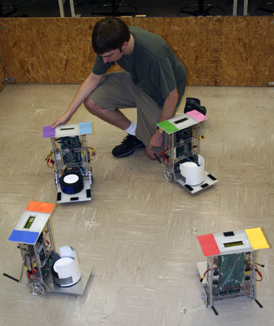 An overhead video camera allows a computer to recognize individual robots by their colored panels.