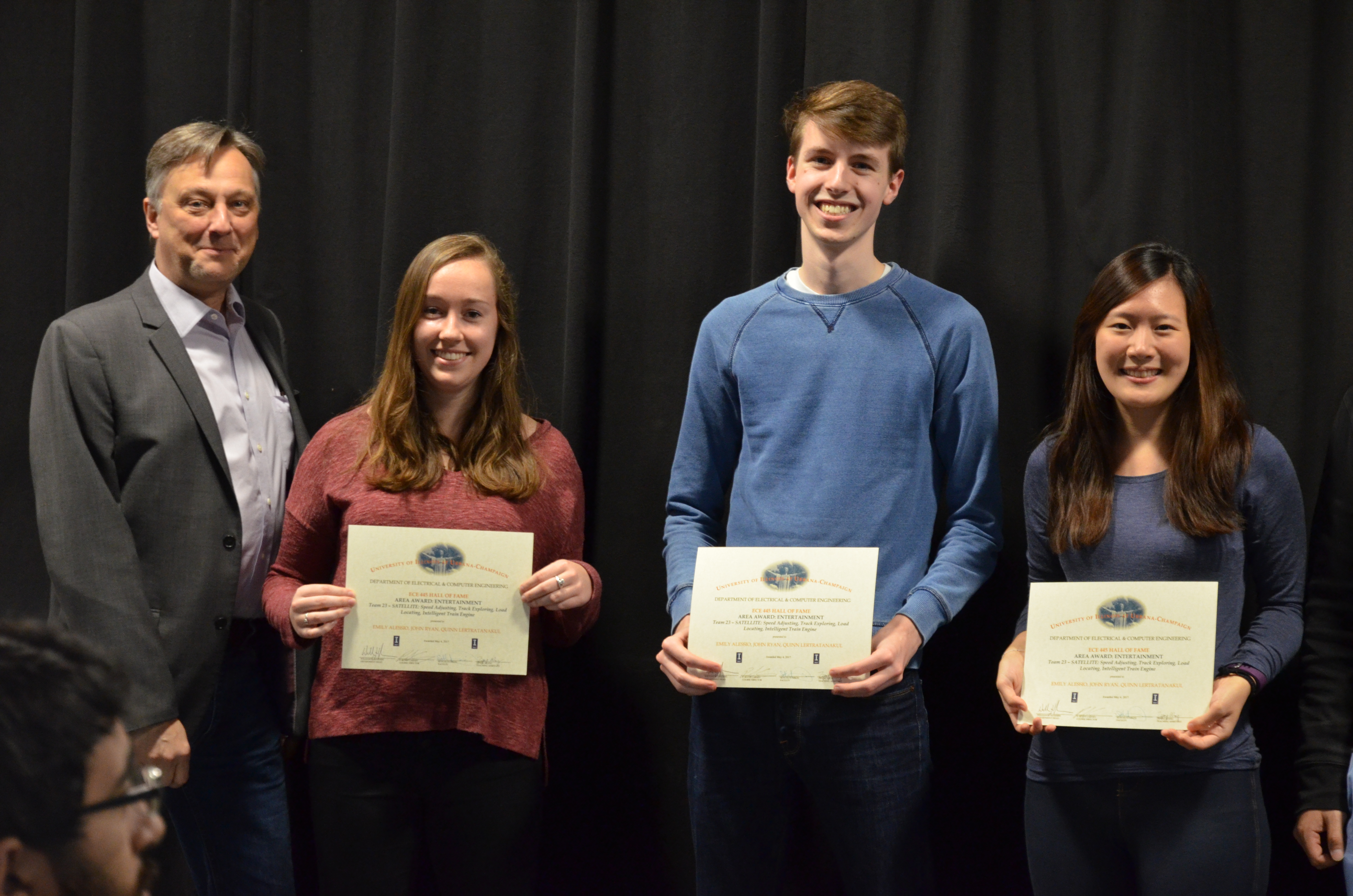 The Area Award for Entertainment was awarded to Emily Alessio, John Ryan, and Quinn Lertratanakul for their 'SATELLITE: Speed Adjusting, Track Exploring, Load Locating, Intelligent Train Engine.' Also pictured : Professor Hutchinson.
