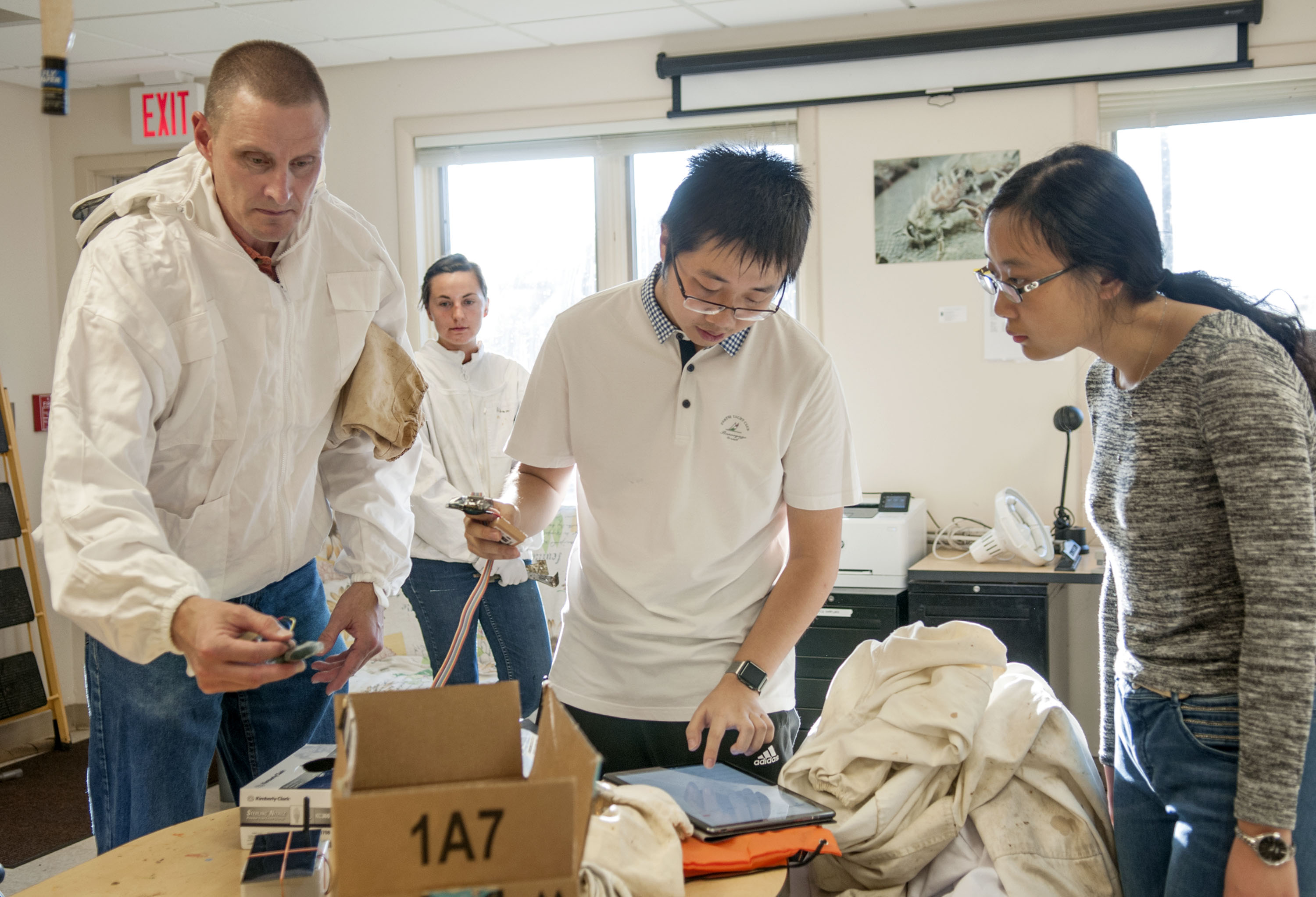 Jimmy He checks the signal using a makeshift application to monitor a data stream, as WaggleNet team members, Chris Schmitz and Xiaolin Wu help to prepare deployment of the wireless monitoring system at the Bee Research Facility in Urbana. Beekeeper Ali Sankey (background left) is the lab manager and the team's first client.